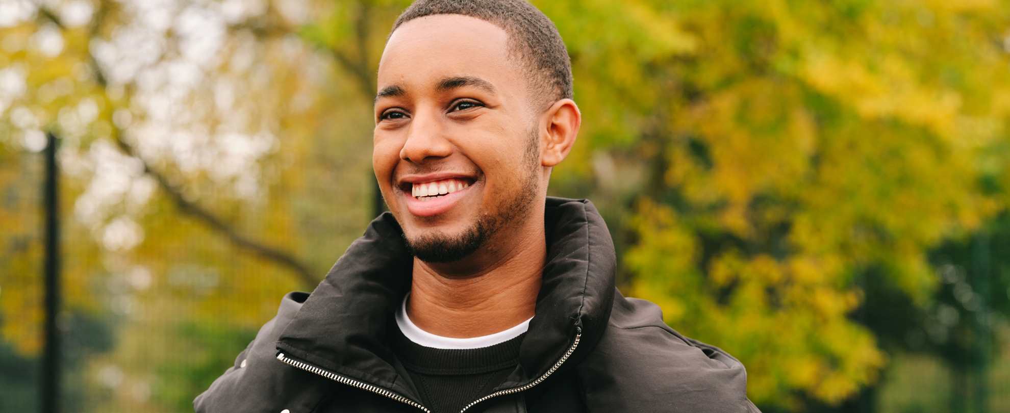 A young Black man smiling in the park.